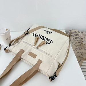 Detailed macro shot of beige canvas tote bag with khaki straps and black Summer embroidery