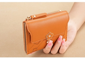 Detail of orange floral embossed leather wallet featuring a gold flower clasp and zipper