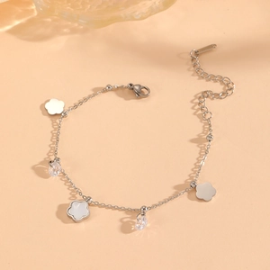 Silver flower charm bracelet with white shell petals and crystals on a peach background