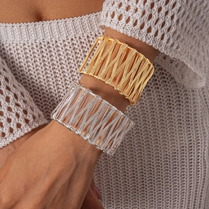 Detail of gold and silver wire-wrapped wide cuff bracelets on model with knitwear