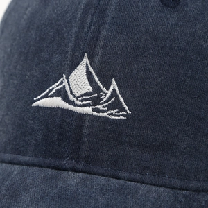 Detailed close-up of mountain peak embroidery on washed navy blue cotton baseball cap