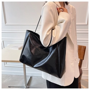 Model wearing a large black leather tote bag over a white suit for office commuters