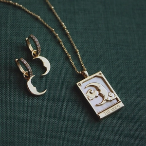 Detail of tarot moon necklace and matching hoop earrings with shell inlay on green fabric