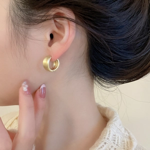 Detailed view of matte golden hoop earrings worn by a model in a minimalist style