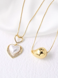 Detailed view of gold plated heart and teardrop pendants with pearl inlay on cross chains