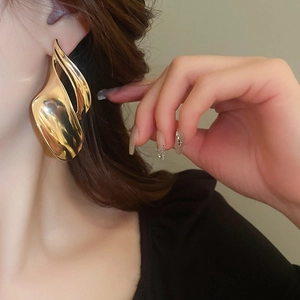 Close-up of large gold wave-shaped metallic earrings worn on model for a modern look