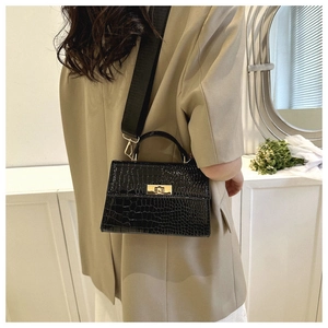 Detail of black crocodile texture handbag with gold twist lock and woven strap worn by model