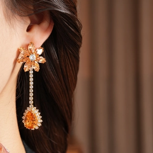 Detail of luxury long drop earrings with orange water-drop gemstone and zircon floral accents