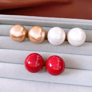 Detailed view of three pairs of minimalist round pearl stud earrings in gold, white, and red