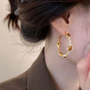 Detail of a C-shape gold earring with amber stones and rhinestones worn by a model