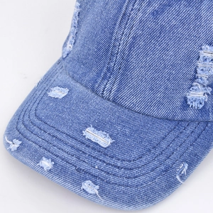 Detailed close-up of distressed denim baseball cap with frayed holes and washed finish