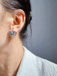 Detail of silver heart stud earrings with hammered lava texture shown on model