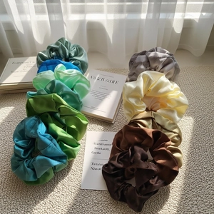 Set of 9 satin silk scrunchies in various earthy and green tones on a neutral background