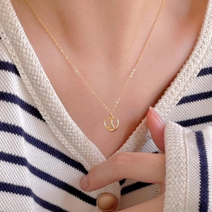 Close-up of a golden pretzel pendant necklace worn by a model in a striped sweater