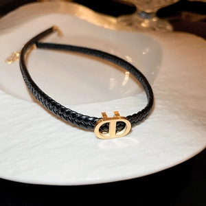Detailed view of black woven leather choker with gold CD metal buckle on white ceramic tray