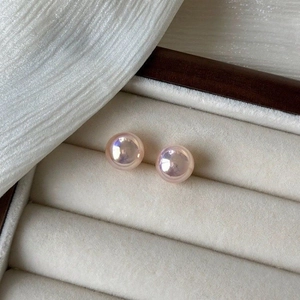 Macro shot of pink iridescent pearl stud earrings resting in a beige jewelry box velvet slot
