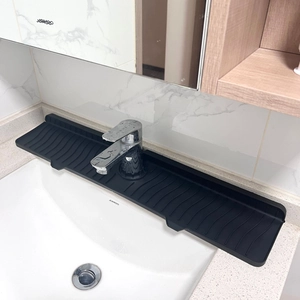 Close-up of black silicone faucet splash guard with drainage grooves on a white sink