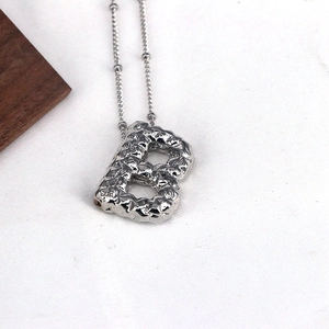 Macro shot of silver letter B pendant with a unique hammered texture on a bead chain