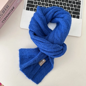Close-up of blue knit wool scarf with a brown label on a minimalist desktop setting