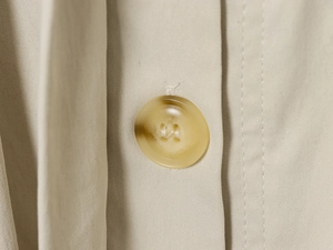 Detailaufnahme eines Vierloch-Harzknopfes an einer khakifarbenen Jacke mit Stehkragen