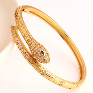 Detail of gold snake bracelet with white zircon pavé and green gem eyes on snake head