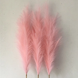 Close-up of three fluffy pink artificial pampas grass stems against a gray wall