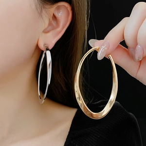 Close-up of twisted geometric oval hoop earrings in polished gold and silver metal finishes