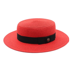 Détail d'un chapeau de paille rouge avec ruban gros-grain noir et insigne doré M chic
