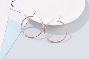 Detailed close-up of rose gold hoop earrings with spiral twisted texture on white porcelain