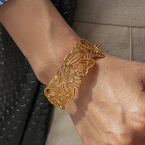 Détail d'un large bracelet doré ajouré avec motifs de fleurs et de papillons
