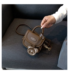 Detailed view of brown PU leather mini crossbody bag with cute bear charm on sofa