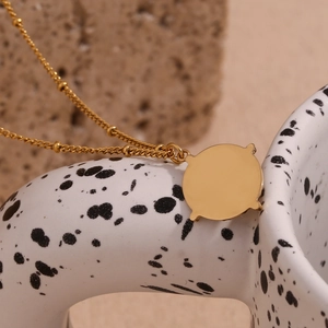 Detail of 18K gold-plated stainless steel necklace with round pendant on stone background