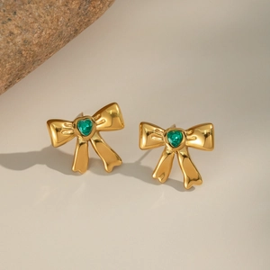 Detailed view of gold bow earrings featuring a green heart-shaped zircon on natural stone