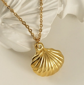 Macro shot of polished gold fan pendant necklace with shell texture on white stone