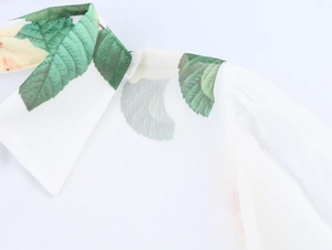 Détail du col d'un chemisier blanc en mousseline avec motifs floraux et feuilles vertes