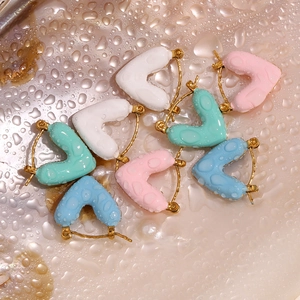 Detail of colorful drip oil heart earrings in white pink blue and green on a wet surface