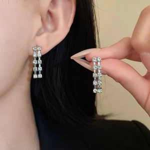 Detail of silver drop earrings with rectangular zircon studs worn by a model in natural light