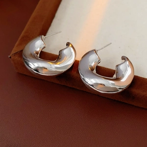 Macro detail of silver C-shaped earrings with irregular lava texture and high mirror finish