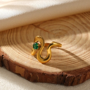 Detailed view of a gold snake-shaped ring with a green gemstone on a rustic wood slice