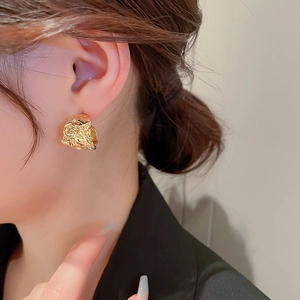 Close-up of a model wearing golden irregular textured C-shaped earrings with liquid metal finish