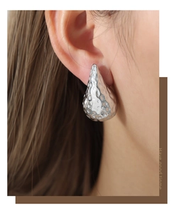 Macro detail of silver-finish teardrop stud earrings with textured hammer finish on model