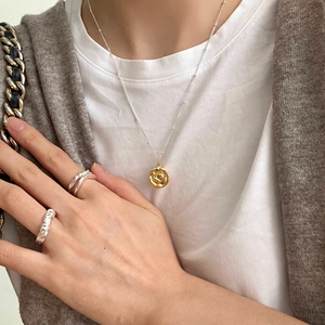 Close-up of a 925 sterling silver necklace with gold pendant and twisted rings on a model