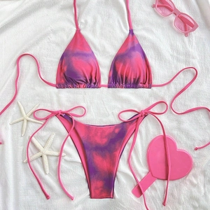 Flat lay of pink and purple tie-dye bikini with summer beach accessories on white fabric