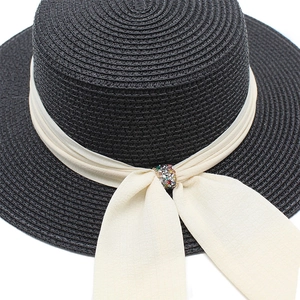 Detail of black straw sun hat with creamy chiffon ribbon and colorful rhinestone buckle