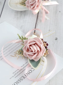 Detailed view of a pink rose wrist corsage with golden leaves and satin ribbon ties