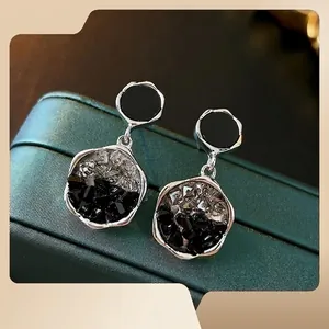 Irregular crystal drop earrings with silver pins and black stones on a jewelry box