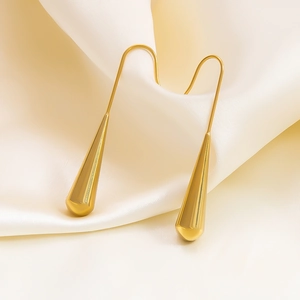 Macro detail of gold teardrop earrings hanging on elegant off-white silk fabric