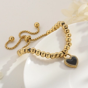 Bracelet de perles dorées avec pendentif cœur noir posé sur un bol en céramique