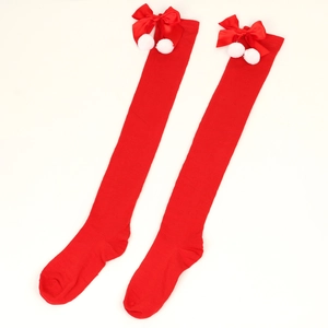 Detail of red knitted over-knee Christmas socks with satin bows and white pompoms