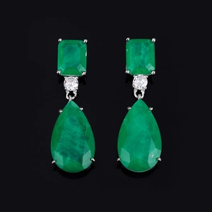 Close-up of emerald green pear-cut drop earrings with silver prongs on black background